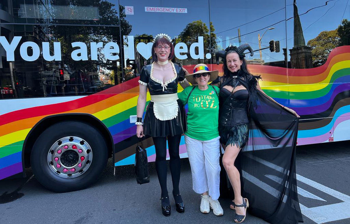 Miss Emm, Hell for Leather, and a fellow Pride March participant in front of a Pride Bus.